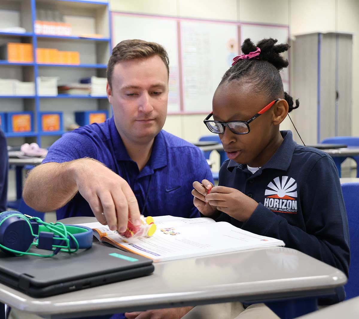HSA Teacher smiles while kneeling beside a young student in a classroom setting.